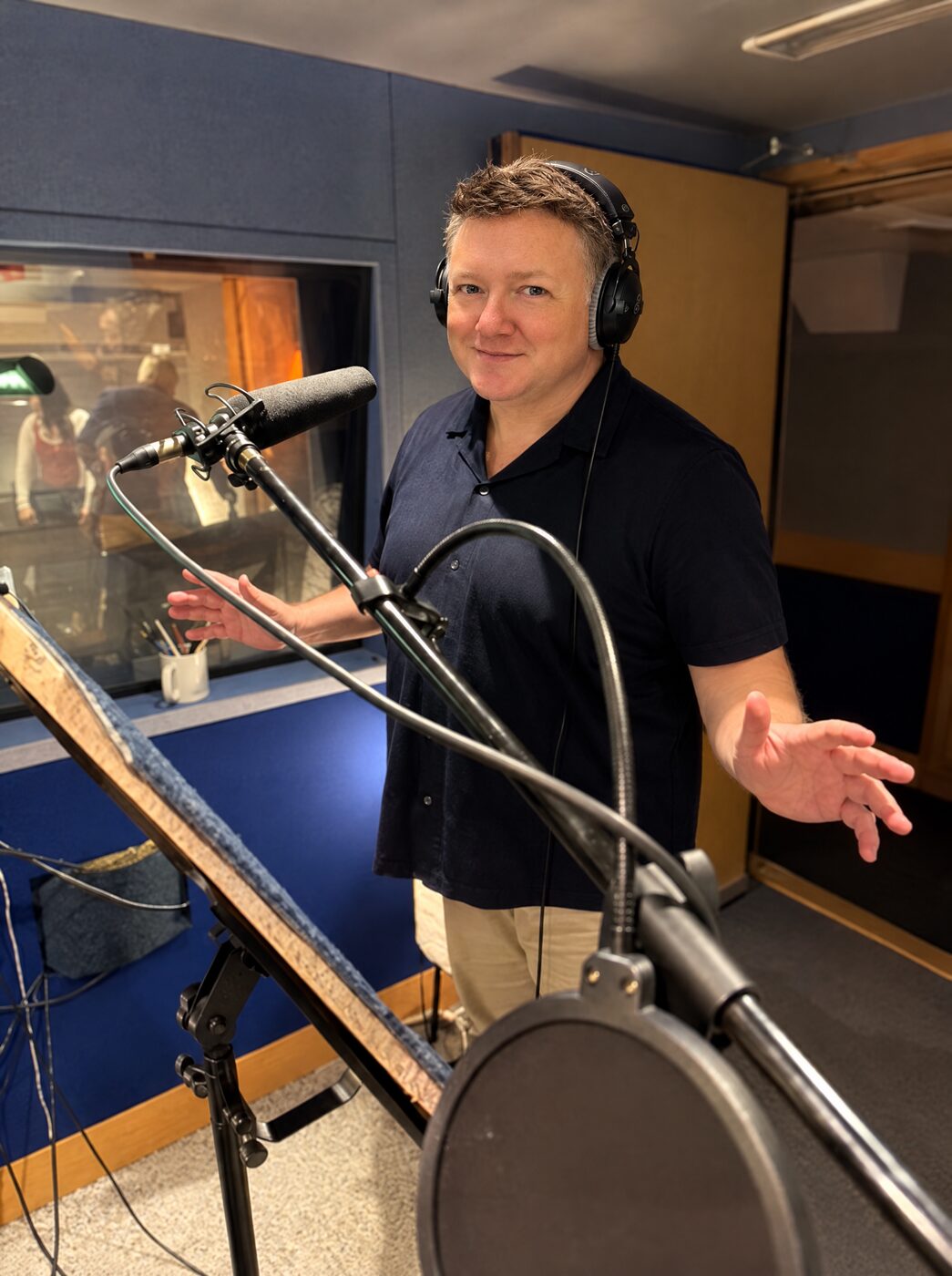 Rob Freeman in a recording booth wearing headphones, standing at the microphone